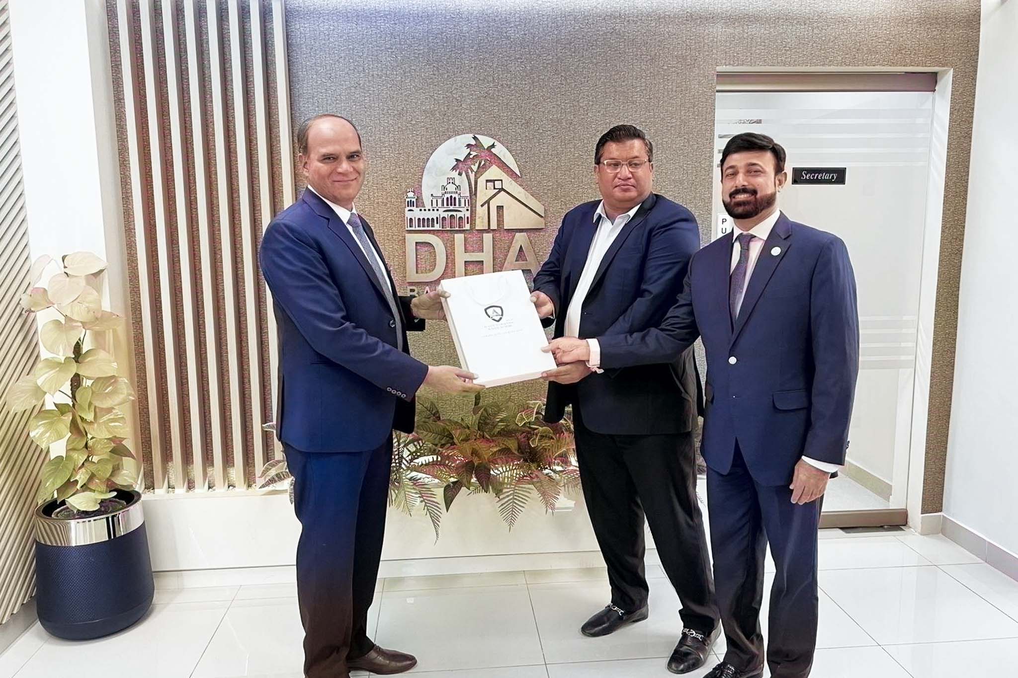 Formal document handover at DHA office; three men in suits participate in official exchange.