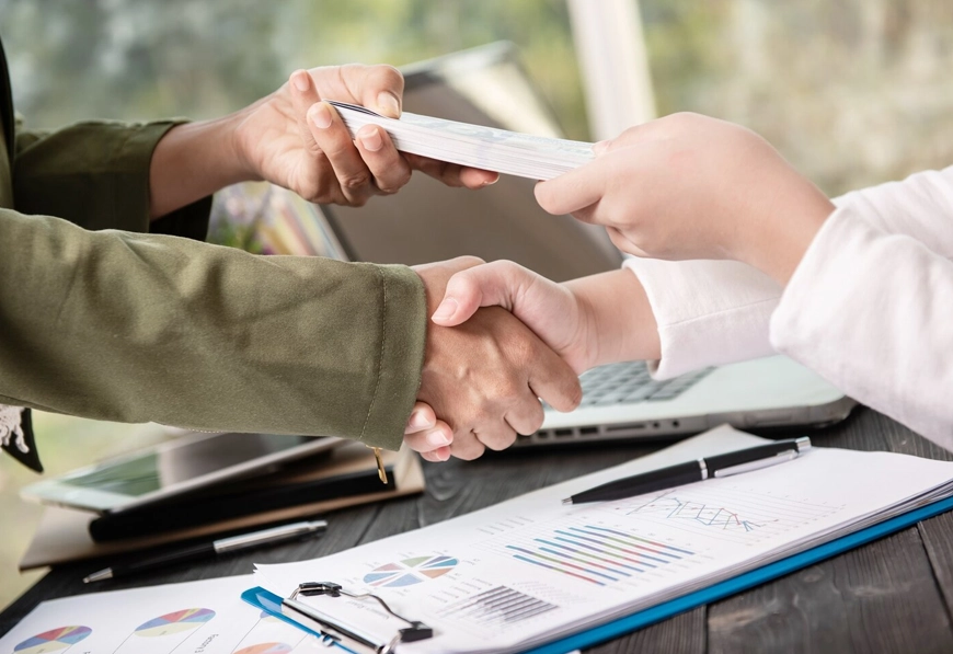 AIBN professionals exchanging check and handshake over financial documents, symbolizing strategic deal-making and trust.