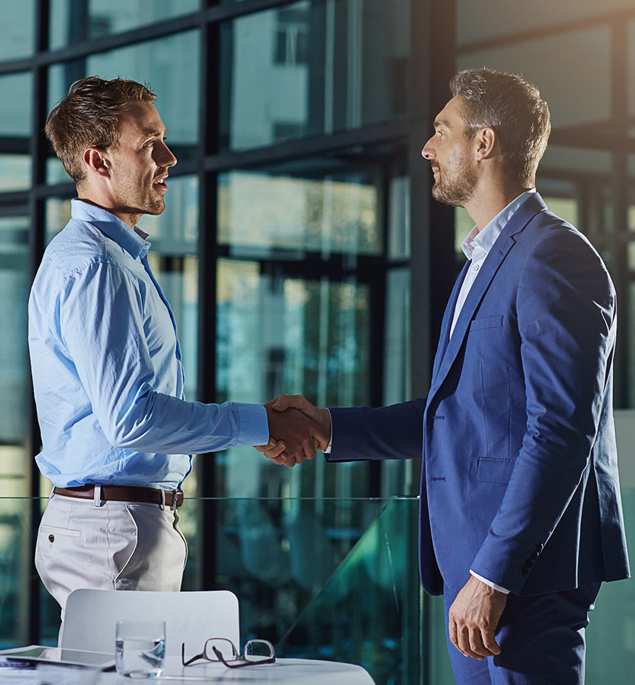 Two businessmen shaking hands in a modern office—symbolizing trust, partnership, and global business collaboration