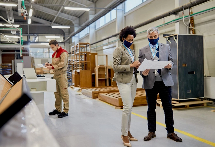 AIBN team reviewing blueprint in manufacturing facility, symbolizing strategic planning and supply chain coordination.